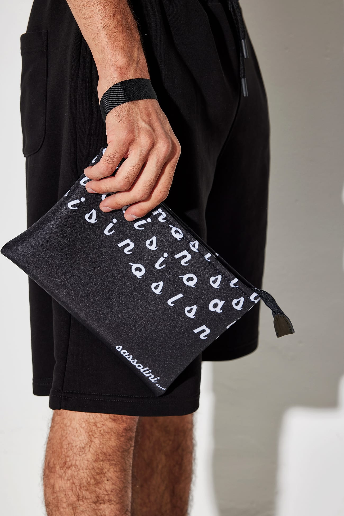 Pochette nera con pattern del wordmark Sassolini, dettaglio mano